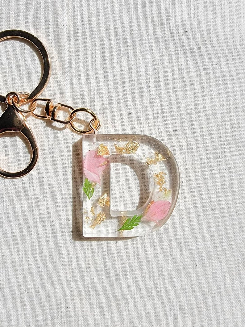 pink flower petals and gold flakes with green leaves. Clear resin letter keychain