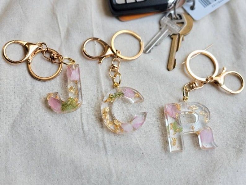 Pink flower petals and gold flakes in clear letter keychain. gold clasp keychain